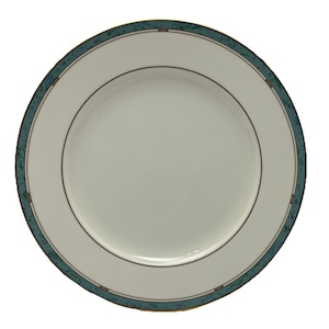 May include: A white ceramic plate with a teal and brown patterned border. The plate has a thin black line near the center and a teal border with a repeating geometric design. This plate is suitable for serving food.