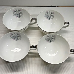 May include: Set of four white ceramic teacups with silver trim and a floral design. Each cup has two handles.