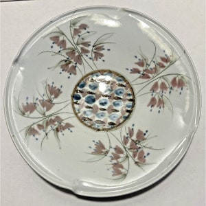 May include: White ceramic plate with a decorative design of pink and blue flowers and a gold and blue center circle.