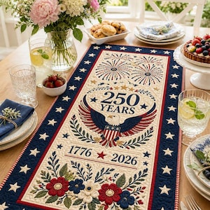 Könnte beinhalten: Patriotischer Tischläufer mit cremefarbenem Mittelteil, der einen Adler, Feuerwerk und den Text "250 YEARS 1776-2026" zeigt. Er hat einen marineblauen Rand mit weißen Sternen und roten Akzenten. Blumen- und Sterndetails.