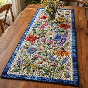 May include: A rectangular floral table runner featuring a vibrant meadow design with red poppies, blue cornflowers, and daisies. The runner has a blue border and is placed on a wooden table. The runner is approximately 60 inches long.