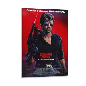 May include: A framed movie poster for "Cobra" featuring Sylvester Stallone. The poster has a red background with Stallone in a black shirt and sunglasses, holding a gun. Text includes "Crime is a disease. Meet the cure."