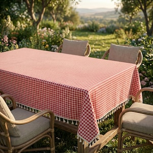 Peut inclure: Une nappe rectangulaire ornée d'un motif à carreaux vichy rouge et blanc. Les bords du tissu sont agrémentés d'une frange décorative composée de petits pompons blanc cassé suspendus tout autour du pourtour de la nappe.