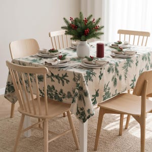 May include: A rectangular tablecloth with a green pine branch pattern on a cream background, covering a dining table with four light wood chairs. The table is set with white plates, napkins, silver rings, a white vase, and a red pillar candle.