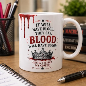 Puede incluir: Una taza de cerámica blanca con un gráfico rojo de sangre goteando en la parte superior y una ilustración de una corona negra en la parte inferior. El texto dice: IT WILL HAVE BLOOD; THEY SAY, BLOOD WILL HAVE BLOOD. (UNTIL I'VE HAD MY COFFEE) en negro y rojo.