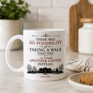 May include: A white ceramic mug featuring black and red text that reads: THERE WAS NO POSSIBILITY of TAKING A WALK THAT DAY. ...so I made ANOTHER COFFEE INSTEAD. JANE EYRE. The design includes a black silhouette of a large house and trees.