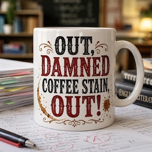 Puede incluir: Taza de café de cerámica blanca con el texto "OUT, DAMNED COFFEE STAIN, OUT!" en letras negras y burdeos. La taza tiene un diseño de mancha de café y un asa curva. La taza está sobre un escritorio con papeles y un bolígrafo.