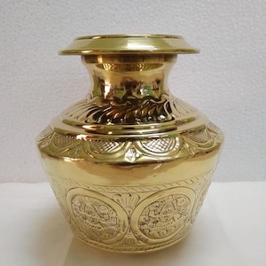 May include: A polished brass pot featuring a wide, flat rim and a rounded body. The surface is decorated with intricate embossed circular patterns depicting figures, surrounded by detailed floral and geometric engravings around the neck.