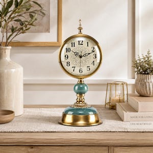 May include: A decorative table clock with a gold-colored frame and base, featuring a teal-colored accent. The clock face has black numerals and hands. The clock is approximately 12 inches tall.