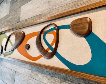 May include: A framed wall art piece with a modern abstract design. The artwork features a beige background with teal, orange, and green abstract shapes. The shapes are outlined in brown wood.