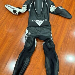 May include: Black and white motorcycle racing suit with the brand name "DAINESE" and "CHINESE" visible. The suit has white accents on the shoulders, arms, and legs. The suit is made of leather and has protective padding.