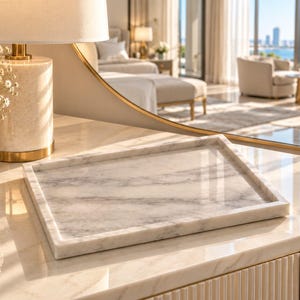 Op de afbeelding: Een rechthoekig dienblad van wit marmer met grijze aders en een opstaande rand. Het dienblad heeft een gladde, gepolijste afwerking en staat op een bijpassend marmeren oppervlak, waarbij het licht over het oppervlak reflecteert.