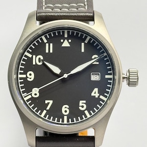 Puede incluir: Un reloj de pulsera de acero inoxidable con esfera negra y números blancos. El reloj tiene una ventana de fecha a las 3 en punto y una correa de cuero marrón con costuras blancas. La caja del reloj mide aproximadamente 4 cm de diámetro.