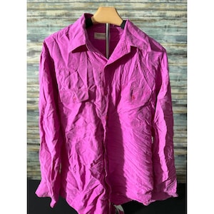 May include: A bright pink button-down shirt with two chest pockets and a collared neckline. The long-sleeved shirt is made of a lightweight fabric and is hanging on a wooden hanger.