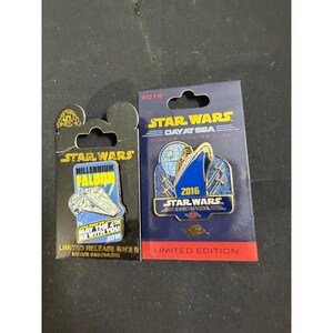May include: Two Star Wars themed metal pins on display cards. The left pin features the Millennium Falcon with text reading Star Wars Millennium Falcon May The 4th Be With You 2016. The right pin shows a cruise ship with the text Star Wars Day At Sea 2016.