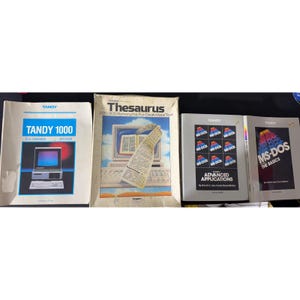 May include: Four vintage Tandy computer manuals including The Complete Guide to the TANDY 1000, a Thesaurus for DeskMate Text, MS-DOS Advanced Applications, and MS-DOS The Basics. These softcover books feature technical graphics and white covers.