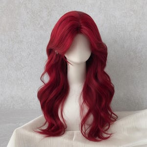 Peut inclure: Perruque rouge longue et ondulée, coiffée sur une tête de mannequin. La perruque présente une raie sur le côté et de longues couches fluides. La couleur rouge vif est uniforme, créant un look audacieux. La perruque est présentée sur une surface blanche.