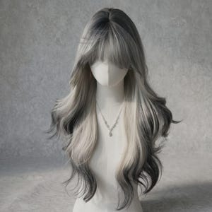 Pode incluir: Uma peruca longa e ondulada com uma transição de raízes cinza-escuras que se mistura com um tom loiro acinzentado mais claro. O cabelo é estilizado com caracóis suaves e volumosos e inclui uma franja completa que emoldura a testa, num manequim.