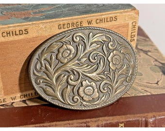 Hebilla de cinturón ovalada de latón con grabado floral estilo western vintage.