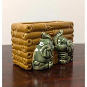 May include: A rectangular ceramic planter featuring a brown bamboo-style textured exterior. Two sculpted green elephants are attached to the front, with one elephant facing forward and the other turned slightly to the side, both with raised trunks.