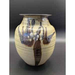 May include: A ceramic vase with a rounded body and a flared rim, featuring a cream-colored base with horizontal ridges and dark brown, blue, and white abstract brushstroke patterns that wrap around the exterior surface of the vessel.