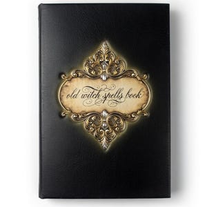 Puede incluir: Un libro negro con las palabras "old witch spells book" en escritura elegante. La portada del libro presenta un marco decorativo dorado y plateado con detalles ornamentados. La portada tiene una apariencia texturizada.