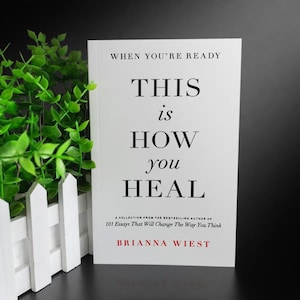May include: A book titled "This is How You Heal" by Brianna Wiest. The cover is white with black text, including the title and the phrase "When You're Ready." The book is a collection of essays.