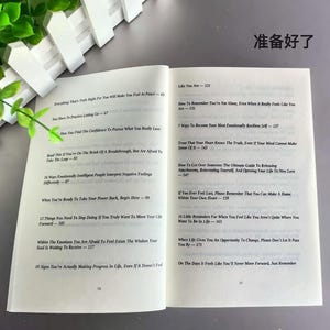 May include: Open book with text on white pages. The left page lists titles like "Everything That's Right For You Will Make You Feel At Peace." The right page includes titles such as "Like You Are." The book is open on a light gray surface.