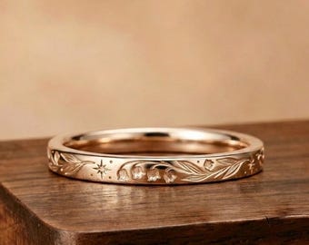 Può includere: Un anello a fascia in oro rosa caratterizzato da un motivo inciso di delicati fiori di mughetto, foglie sottili e piccole stelle a quattro punte che circondano l'intera superficie esterna dell'anello con una finitura lucida.