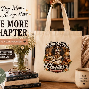 Op de afbeelding: Een beige canvas tas met een kleurrijke afbeelding van een Cavalier King Charles-spaniël die in een bibliotheek zit met boeken, een koffiekopje en een wereldbol. De tekst luidt One More Chapter en Dog Mom Maffia, met bloemaccenten.