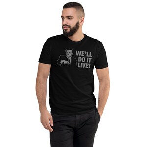 Op de afbeelding: Zwart t-shirt met een grijze afbeelding van een man die wijst, met de tekst "WE'LL DO IT LIVE!". Het shirt is gemaakt van zacht materiaal en heeft een klassieke ronde hals.