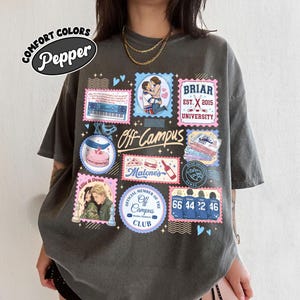Peut inclure: Un t-shirt gris anthracite à manches courtes orné d'un collage de timbres graphiques colorés et de texte. Les motifs incluent des illustrations d'un couple, d'un clavier, d'une pizza, d'une bouteille et de maillots de hockey avec le texte Off Campus.
