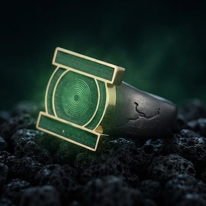 May include: A ring featuring a dark, textured band and a prominent, rectangular green face. The face displays a circular, concentric ring pattern in a lighter green shade, framed by a gold-toned metal border that extends horizontally.