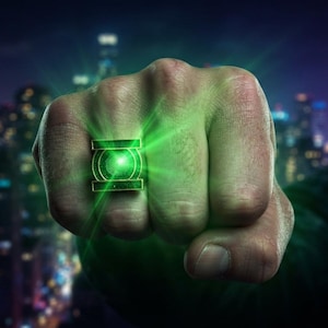 May include: A metallic ring featuring a prominent green circular emblem with a central glowing light, set within a rectangular frame. The ring displays a vibrant green radiance that emanates from the center, casting a bright light outward.