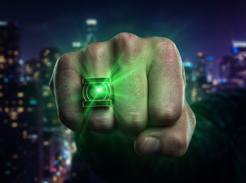 May include: A metallic ring featuring a prominent green circular emblem with a central glowing light, set within a rectangular frame. The ring displays a vibrant green radiance that emanates from the center, casting a bright light outward.