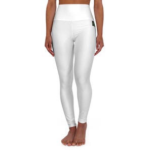 Könnte beinhalten: Weiße Leggings mit hohem Bund. Die Leggings bestehen aus einem glatten, blickdichten Material. Ein kleines, dunkelgrünes und schwarzes Etikett ist oben links an der Leggings sichtbar. Die Leggings sind figurbetont und reichen bis zu den Knöcheln.