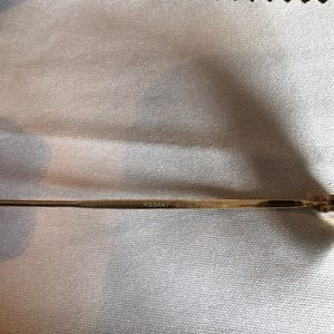 May include: Close-up of a gold-colored eyeglass arm. The text "RB3447 51" is printed on the arm. The background is a light-colored, textured fabric.