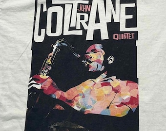 Puede incluir: Una camiseta blanca con un estampado gráfico de un músico tocando el saxofón. El diseño incluye el texto John Coltrane Quintet en letras negras y rosas. La figura está representada en un estilo de mosaico abstracto y colorido.