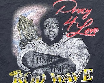 Puede incluir: Una camiseta negra con un estampado gráfico de una persona con barba, manos juntas en oración y el texto "Pray 4 Love" en letra roja. La persona tiene "HARD TIMES" tatuado en los antebrazos. El nombre "ROD WAVE" aparece en color amarillo.