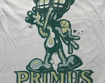 Puede incluir: Una camiseta gris claro con un estampado gráfico en verde oscuro y amarillo pálido de una criatura estilizada de ojos saltones, extremidades largas y pies grandes. Debajo de la criatura, la palabra PRIMUS está impresa en letra negrita.
