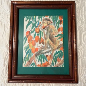 May include: A framed print featuring a monkey in a tree, surrounded by orange fruit and green leaves. The artwork is set against a green mat and framed in a dark brown bamboo-style frame. The print has a vintage aesthetic.