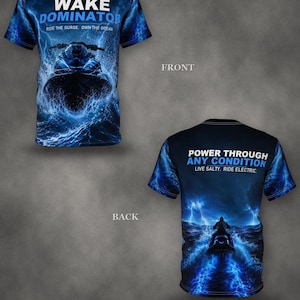 May include: A short-sleeved t-shirt featuring a blue and black graphic of a jet ski on water. The front displays the text WAKE DOMINATOR RIDE THE SURGE. OWN THE OCEAN. The back features the text POWER THROUGH ANY CONDITION LIVE SALTY. RIDE ELECTRIC.