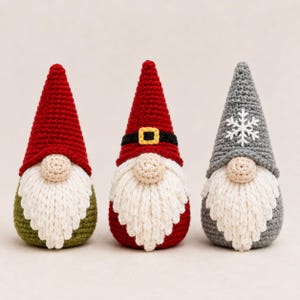 May include: Three crocheted gnome figurines with pointed hats and white yarn beards. The left gnome has a red hat and olive green body. The center gnome has a red hat with a black and yellow belt. The right gnome has a gray hat with a white snowflake.