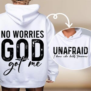 May include: White hoodie with black text on the back that reads "NO WORRIES GOD got me." A smaller circular image shows a hoodie with the word "UNAFAID" and the text "I know who holds tomorrow."