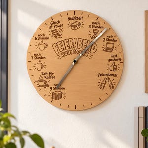 May include: A round wooden wall clock featuring the text FEIERABEND COUNTDOWN in the centre. The clock face includes various icons and German text labels marking time intervals, such as Mahlzeit, noch 3 Stunden, noch 2 Stunden, Fast geschafft, Feierabend, noch 9 Stunden, Zeit für Kaffee, noch 7 Stunden, noch 6 Stunden, and Gleich ist Pause.