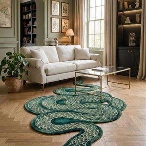 Può includere: Un grande tappeto a forma di serpente arrotolato. Il tappeto presenta un colore verde intenso con un motivo a scaglie color crema più chiaro su tutto il corpo. La testa del serpente è posizionata nella parte anteriore con dettagli del volto.