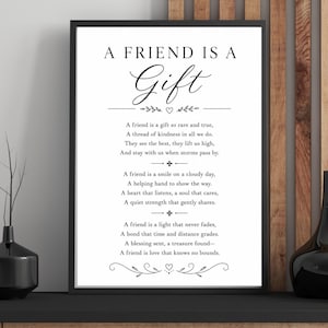 以下が含まれることがあります： 「A FRIEND IS A GIFT」と書かれた黒いフレームのプリント。友情についての詩が書かれており、花やハートの装飾が施されています。このアートワークは黒い棚に飾られています。