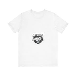 Puede incluir: Camiseta blanca con un gráfico negro y gris. El gráfico presenta el texto "PRESSURE CREATES DIAMONDS" sobre una forma de diamante con bordes puntiagudos. La camiseta está hecha de un material suave.