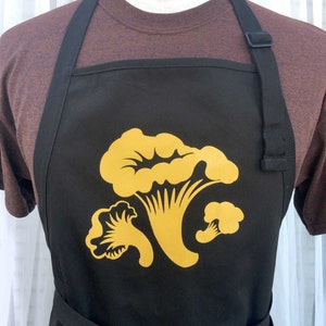 May include: Black apron with adjustable straps and a gold mushroom design.