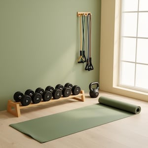 May include: A home gym setup featuring a green yoga mat, dumbbells on a wooden rack, resistance bands, and a kettlebell. The equipment is arranged against a light green wall, with a window in the background.